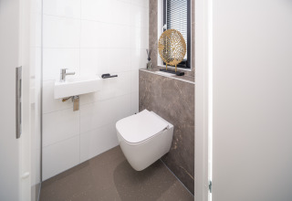 Toilettes de lodge modernes avec WC suspendu, petit lavabo et décoration élégante sur le rebord de fenêtre.