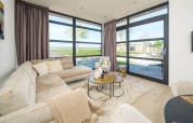 Helles, modernes Wohnzimmer einer Lodge mit großen Fenstern, gemütlichem Sofa und Blick ins Grüne.