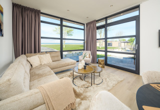 Helles, modernes Wohnzimmer einer Lodge mit großen Fenstern, gemütlichem Sofa und Blick ins Grüne.