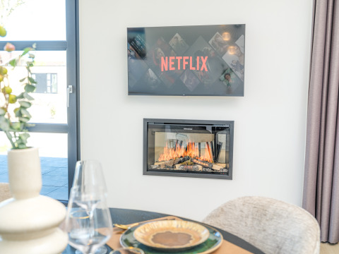 Modernes Lodge-Wohnzimmer mit einem Fernseher, der Netflix zeigt, und einem Kamin darunter an der Wand.