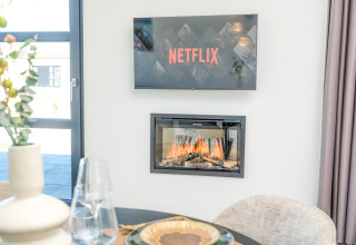 Salon moderne de lodge avec une télévision affichant Netflix au-dessus d'une cheminée chaleureuse et table.