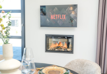 Sala moderna de lodge con televisión mostrando Netflix sobre una chimenea acogedora junto a una mesa.