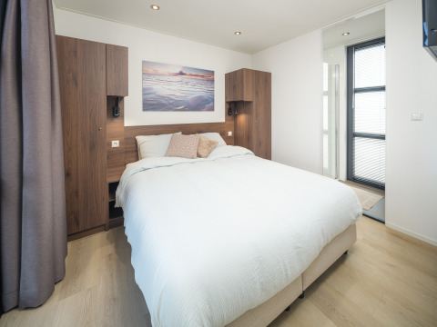 Camera da letto moderna in un lodge con letto matrimoniale, armadi in legno e grande luce naturale.
