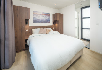 Dormitorio de lodge moderno con cama doble, armarios de madera, buena luz natural y cuadro de playa.