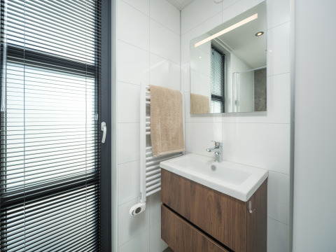 Salle de bain moderne dans un lodge avec lavabo, grand miroir, serviette et fenêtre à stores vénitiens.