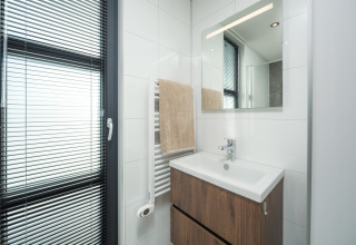 Modernes Badezimmer in einer Lodge mit Waschbecken, Spiegel, Handtuchheizkörper und Fenster mit Jalousien.