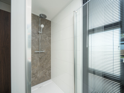 Moderne Dusche in einer Lodge mit Glaswand, weißen Fliesen und Fenster mit Jalousien.