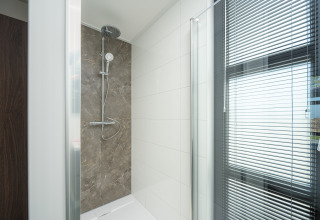 Moderne Dusche in einer Lodge mit Glaswand, weißen Fliesen und Fenster mit Jalousien.