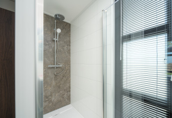 Ducha moderna en un baño de lodge con puerta de cristal, azulejos blancos y ventana con persianas.