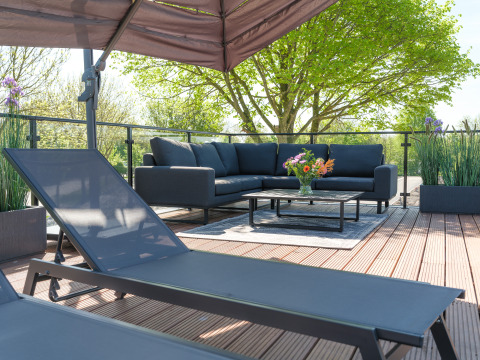 Modernes Lounge-Areal im Freien bei einer Lodge mit Sofa, Tisch, Blumen und Pflanzen bei sonnigem Wetter.