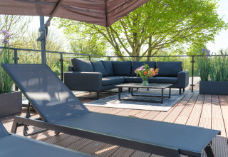 Modernes Lounge-Areal im Freien bei einer Lodge mit Sofa, Tisch, Blumen und Pflanzen bei sonnigem Wetter.