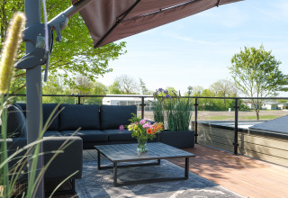 Terrasse sur le toit de la Villa L-Meerzicht avec canapé, parasol et vue dégagée sur la verdure.