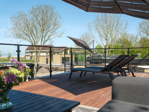 Terrasse sur le toit de la Villa L-Meerzicht avec chaises longues, fleurs et vue sur maisons et arbres.