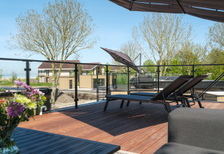 Terrasse sur le toit de la Villa L-Meerzicht avec chaises longues, fleurs et vue sur maisons et arbres.