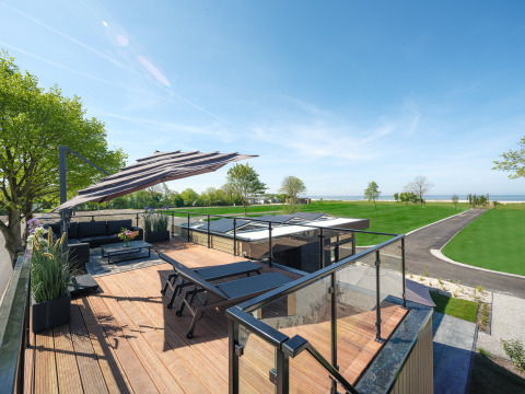 Terrasse sur le toit de la Villa L-Meerzicht avec salon, chaises longues et vue sur la mer verdoyante.