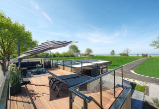 Terrasse sur le toit de la Villa L-Meerzicht avec salon, chaises longues et vue sur la mer verdoyante.