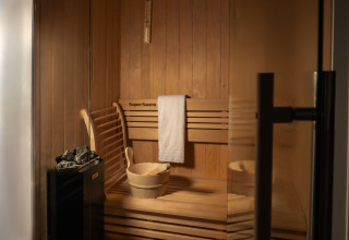 Wooden sauna with towel, bucket, and stones in Villa Meerzicht at MarinaPark Beach Resort Soal, Netherlands.