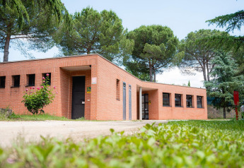 Bakstenen gebouw bij Camping Il Poggetto in Italië, omgeven door bomen, gefotografeerd vanaf het gras.