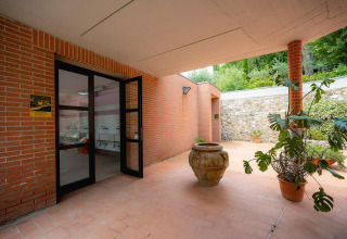 Pasillo exterior con paredes de ladrillo, puertas de vidrio, plantas en maceta y lavamanos en Camping Il Poggetto.