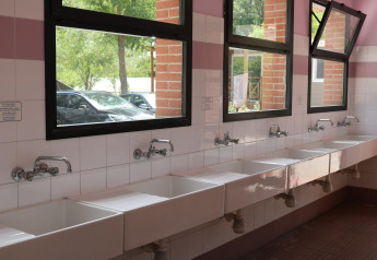 Rangée de lavabos blancs sous des fenêtres ouvertes dans la salle de bains commune au Camping Il Poggetto, Italie.