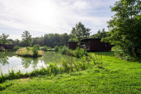 Uitzicht op een vijver, eilandje en houten lodges bij The Leaf by YourNature, België.
