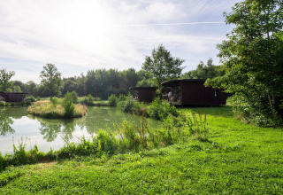 Uitzicht op een vijver, eilandje en houten lodges bij The Leaf by YourNature, België.