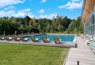 Buitenzwembad bij een glamping-accommodatie, houten ligstoelen op terras, gasten relaxen in de zon.