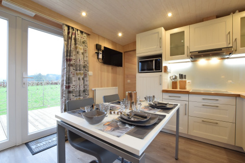 Cucina moderna e zona pranzo a La roulotte des Ardennes, Belgio, con tavolo apparecchiato e vista panoramica.