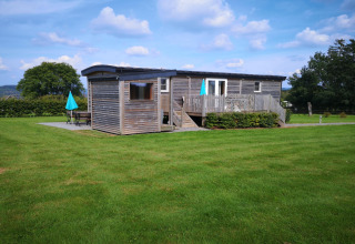 Un'accogliente lodge in legno su un prato verde sotto cielo azzurro a La roulotte des Ardennes, Belgio.