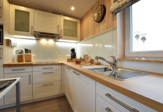 Cucina moderna con mobili bianchi, piani in legno e grande finestra a La roulotte des Ardennes, Belgio.
