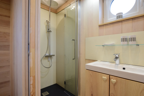 Bagno moderno a La roulotte des Ardennes in Belgio con doccia, lavabo e finiture in legno chiaro.