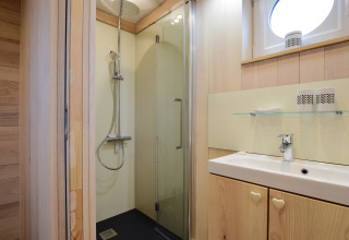 Bagno moderno a La roulotte des Ardennes in Belgio con doccia, lavabo e finiture in legno chiaro.
