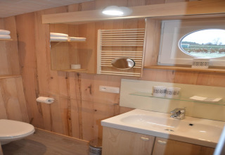 Bagno con pannelli in legno, lavandino, specchio, asciugamani e finestra rotonda a La roulotte des Ardennes, Belgio.