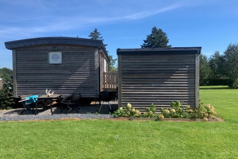 Immagine del lodge La roulotte des Ardennes in Belgio, con casette di legno, sedie e prato verde.