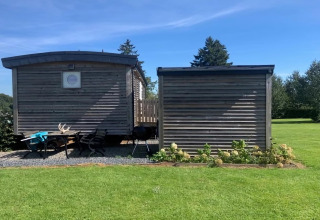 Immagine del lodge La roulotte des Ardennes in Belgio, con casette di legno, sedie e prato verde.
