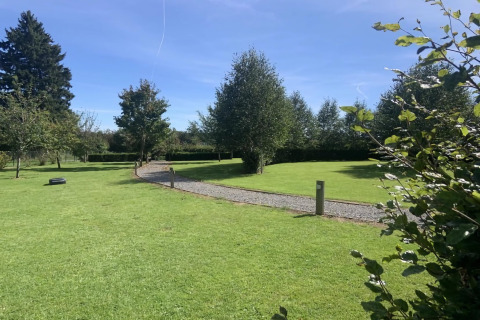 Prato verde con sentiero di ghiaia e alberi presso La roulotte des Ardennes in Belgio in una giornata soleggiata.