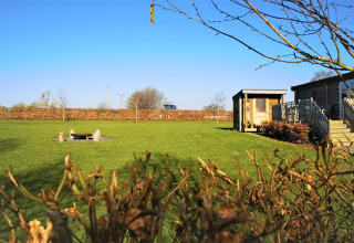 Prato verde con focolare e casetta in legno a La roulotte des Ardennes in Belgio sotto cielo azzurro.