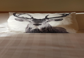 Un cuscino con una stampa di cervo su un letto nel lodge La roulotte des Ardennes in Belgio.