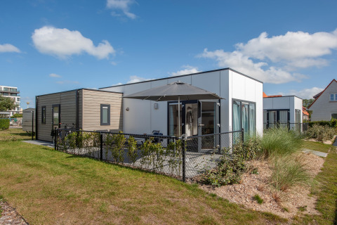 Moderne lodge in Breeduyn Village 3 met terras, zwart hek en parasol op een zonnige dag
