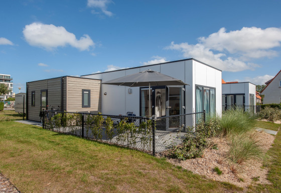 Moderne lodge in Breeduyn Village 3 met terras, zwart hek en parasol op een zonnige dag
