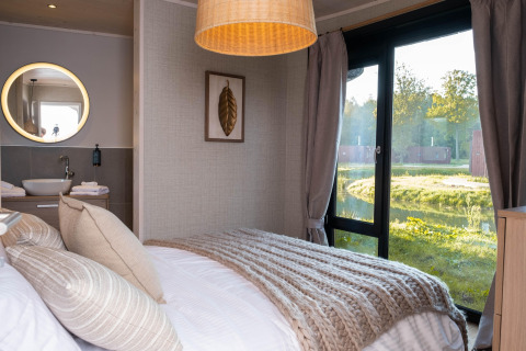 Knusse glampingaccommodatie met comfortabel bed, eigentijds interieur en groot raam met uitzicht op de natuur.