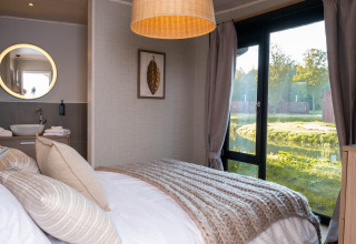 Knusse glampingaccommodatie met comfortabel bed, eigentijds interieur en groot raam met uitzicht op de natuur.