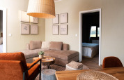 Modern glamping accommodation interior with cozy sofa, orange chairs, wooden decor, and visible bedroom.