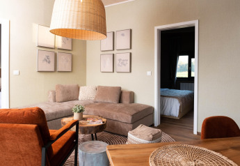 Modern glamping accommodation interior with cozy sofa, orange chairs, wooden decor, and visible bedroom.