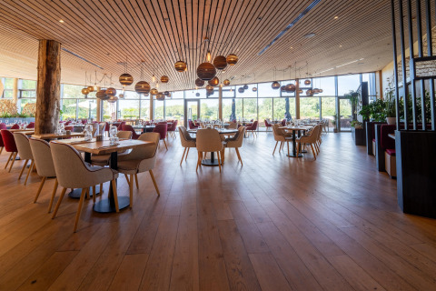 Ruim restaurant met houten interieur en grote ramen bij een luxe glampingaccommodatie in de natuur.