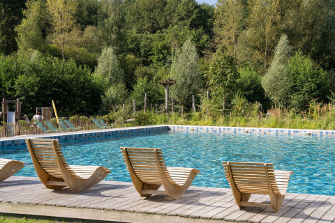Scenic outdoor swimming pool with unique wooden loungers, nestled in lush greenery at a glamping site.