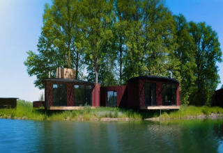Een moderne lodge aan het meer, omgeven door groene bomen en blauwe lucht bij The Leaf by YourNature, België.