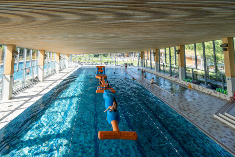Indoor swimming pool with inflatable obstacle course, families and kids enjoying a glamping resort.