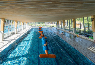 Piscina cubierta con circuito inflable y familias disfrutando de un alojamiento glamping moderno.