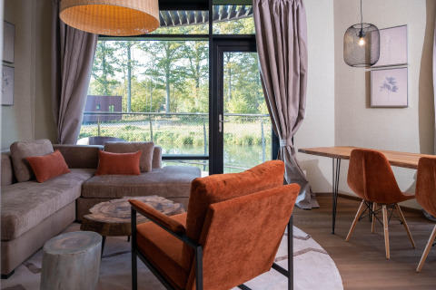 Gezellige glampingruimte met grote ramen, uitzicht op de natuur en stijlvol moderne meubels.